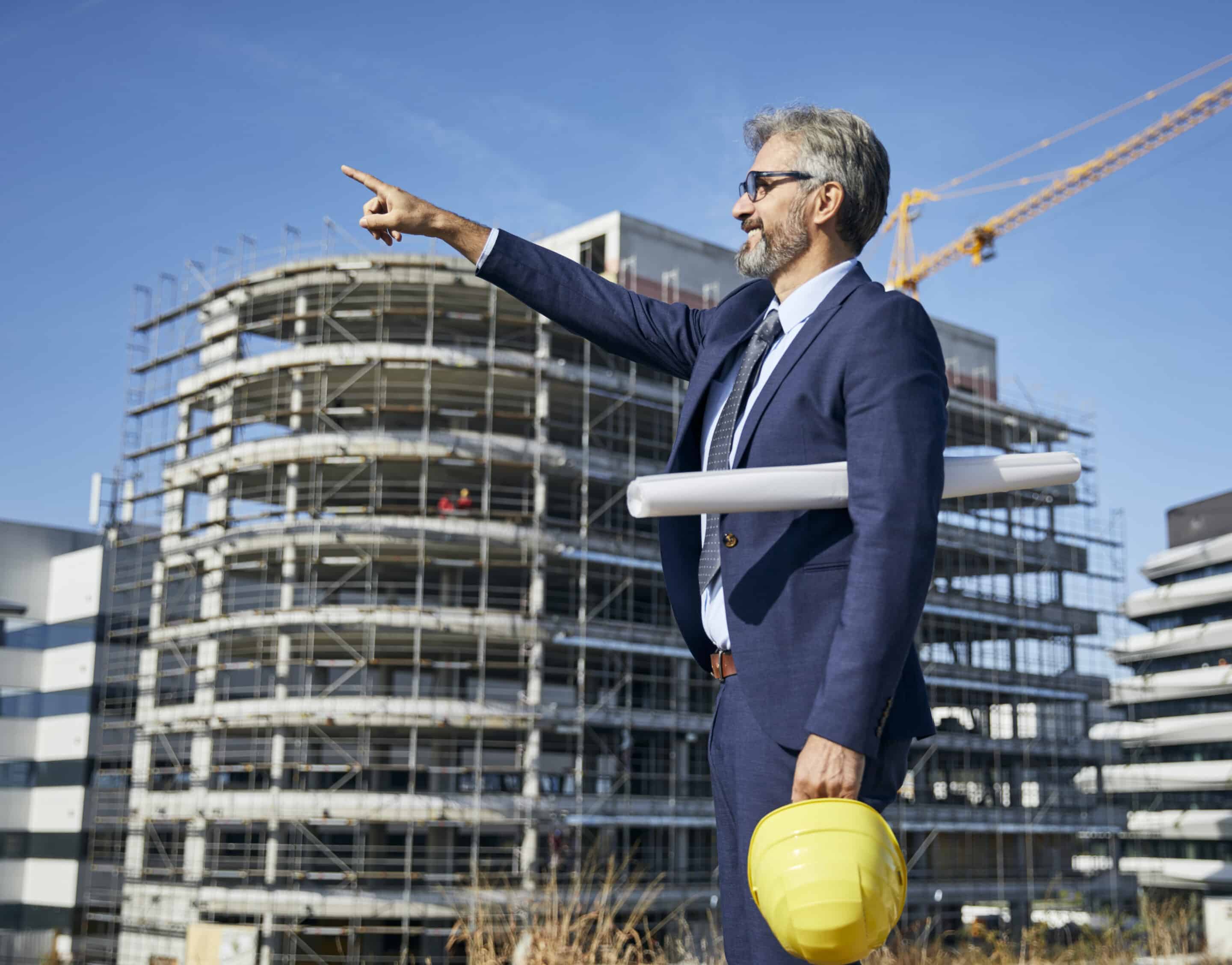 senior businessman architect wearing a protective helmet using a tablet and a blueprint on the construction site